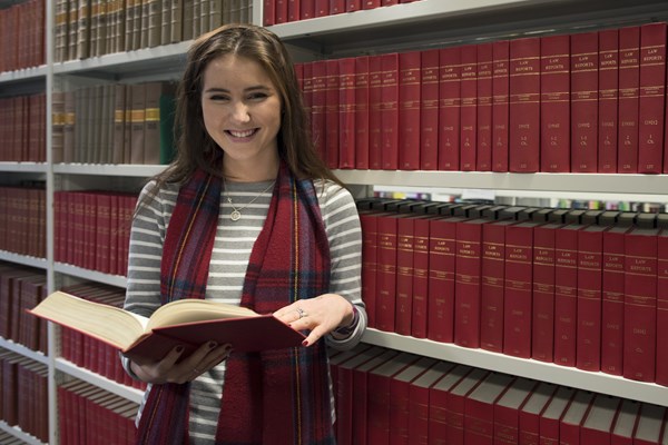Smiling student standing infront of library book case holding a book