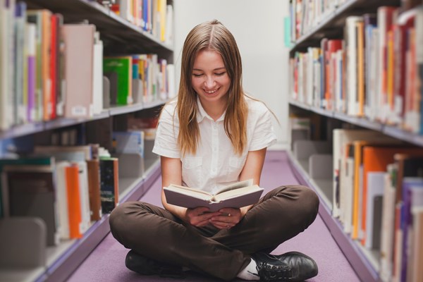 Student sat on library floor reading a book